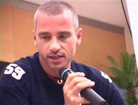 a man holding a microphone in his right hand and wearing a black shirt with white letters on it
