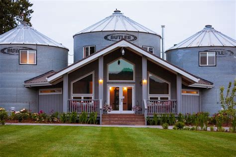 an image of a house with three silos in the back ground and flowers on the front lawn