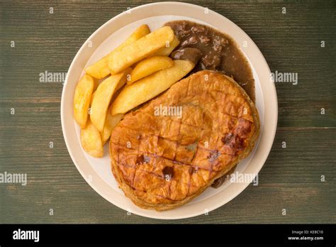 Beef Steak Pie With A Puff Pastry Crust Top And Chips On A Green Wooden ...