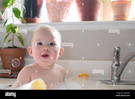 Baby taking bath in the kitchen sink. Child playing with foam and soap ...