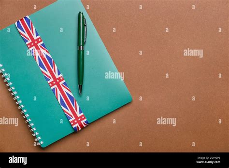 Notebook, pen and ribbon in colors of UK flag on color background. Concept of learning English ...