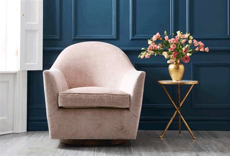 a pink chair next to a gold side table with flowers on it in front of a blue wall