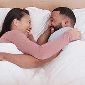 Happy couple, bed and laughing in morning joke, relax or together on funny holiday, weekend or ...