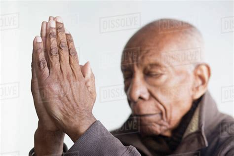 Older Black man praying with hands clasped - Stock Photo - Dissolve