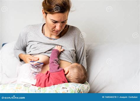 Mother Breastfeeding Her Newborn Baby while Pumping Milk from Her Other ...