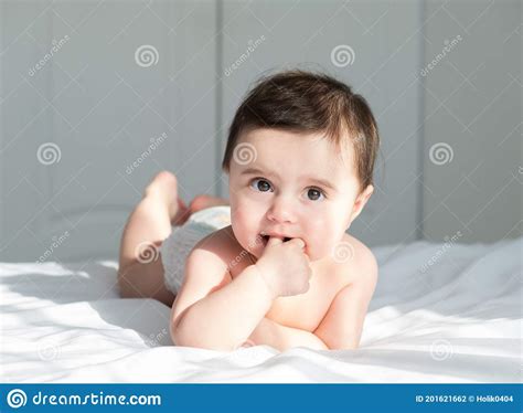 Baby Girl Smiling, Lying on a Bed on White Bedding in White Bodysuit. Sunny Morning with Shadows ...