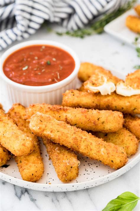 White plate of breaded and coated mozzarella served with marinara sauce.