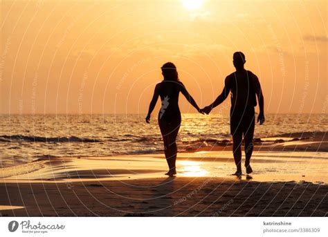 Silhouette of a couple walking at the beach in front of the sunset - a ...