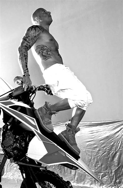 a man with tattoos on his arm standing next to a motorcycle