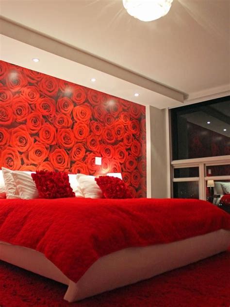 a bed with red sheets and pillows in front of a wall that has roses on it