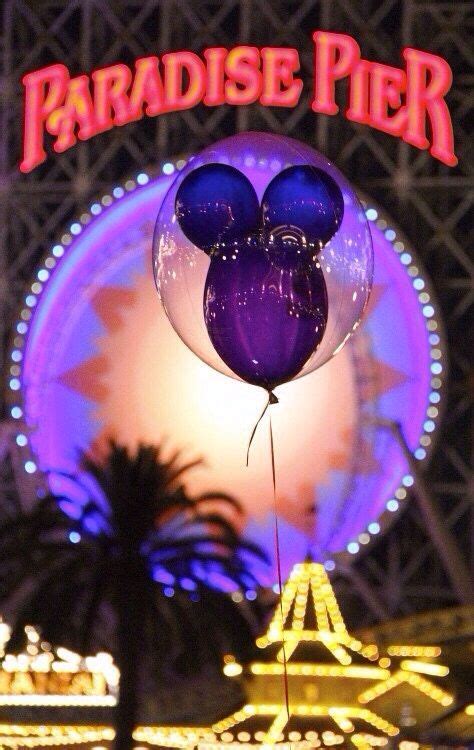 the entrance to paradise pier at night with balloons floating in the air and ferris wheel behind it