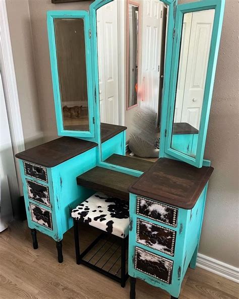 a blue vanity with mirror, stool and cow hide rug on the floor in front ...