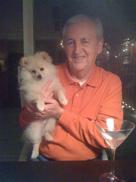an older man holding a small white dog in his arms next to a martini glass