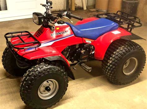 a red four - wheeler parked in a garage next to a blue and white motorcycle