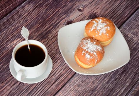 A Cup of Black Hot Coffee and a Plate with Two Fresh Donuts in Powdered Sugar on a Wooden Table ...