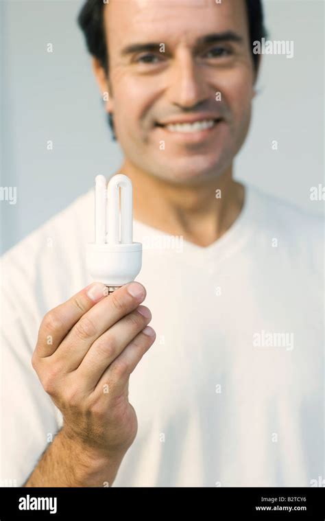 Man holding energy efficient light bulb, smiling at camera Stock Photo - Alamy