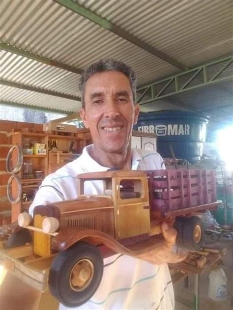 a man holding a wooden toy truck in his hand and smiling at the camera,