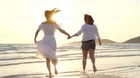 Young Asian lesbian couple running on beach. Beautiful women friends