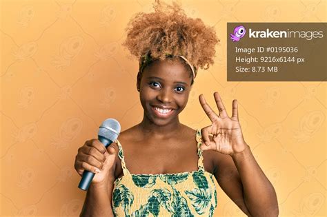 Young african woman with afro hair singing song using microphone doing ...