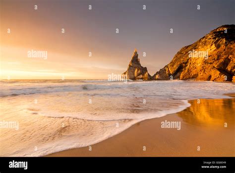Golden reflections of the cliffs on Praia da Ursa beach bathed by ocean