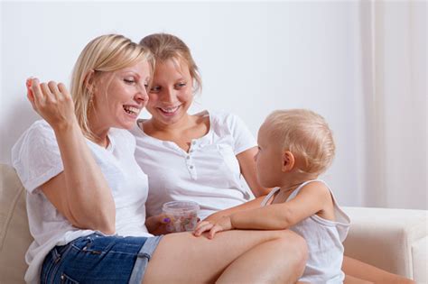 Mother And Children Sitting On Couch Laughing And Eating Sweets Stock