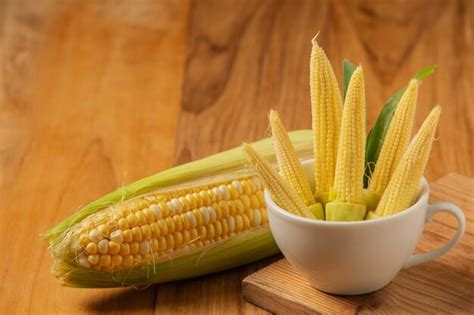Детская кукуруза укладывается в стакан на деревянный пол. | Бесплатно Фото