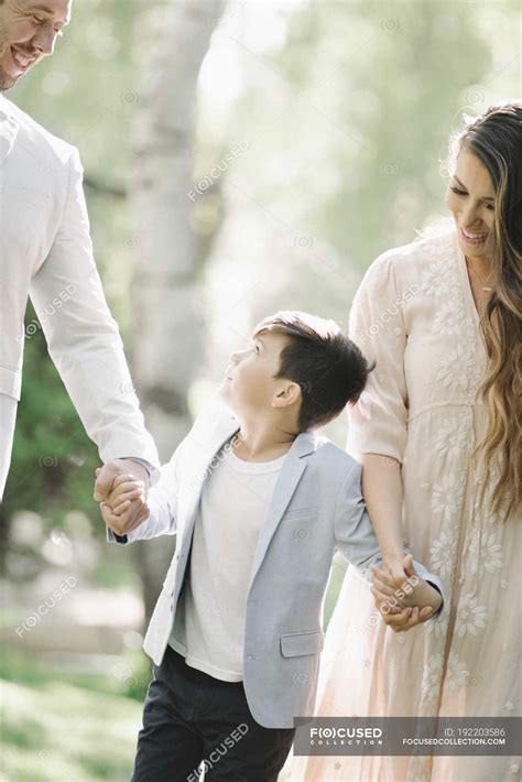 Father, mother and son walking and holding hands in park. — Pre Teen