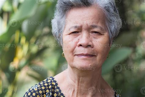 Asain elderly woman smiling and looking at camera while standing in a