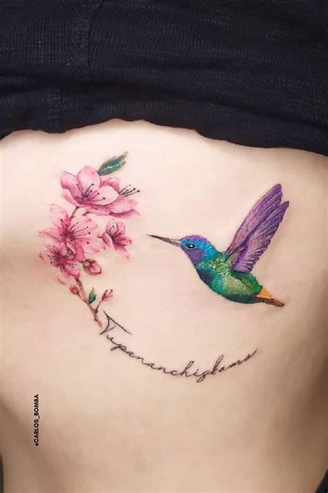 a woman's stomach with a hummingbird and flower tattoo on her side ribcage