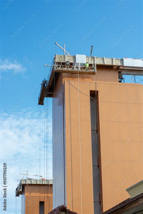 Using a construction gondola lift, workers place panels on a towering ...