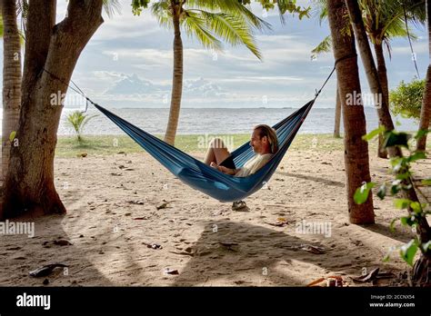 Hammock beach. Man relaxing in a hammock strung between trees on a tropical beach against the ...