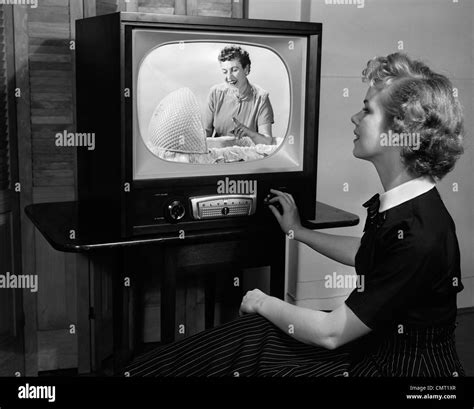 1950s BLONDE WOMAN TURNING DIAL ON TV SET WATCHING PROGRAM ABOUT BABY ...