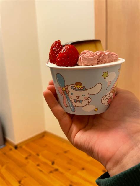 a person holding up a bowl of ice cream with strawberries in it