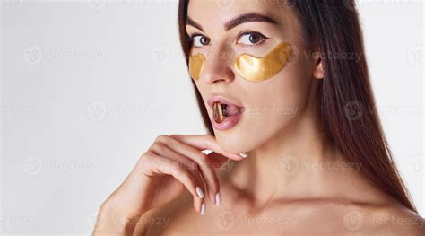 Naked woman in the studio with golden tapes near eyes and with pill in