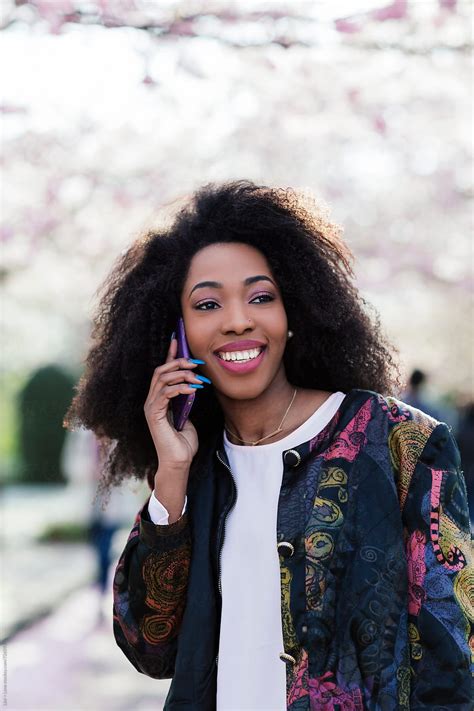 "Young Black Woman Smiling While Talking On The Phone Outdoors" by