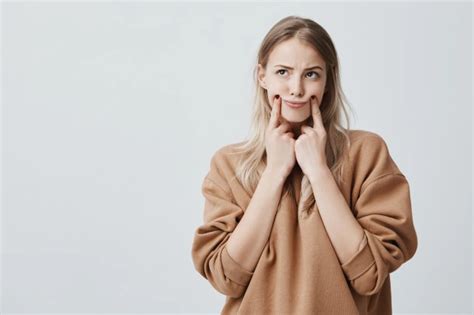 Довольно белокурая женщина делает гримасу, касаясь пальцами ее щек ...