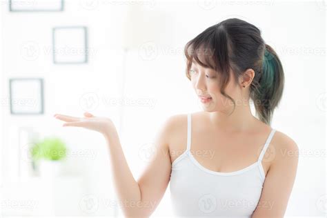 Beautiful young asian woman smiling and showing skin care product for