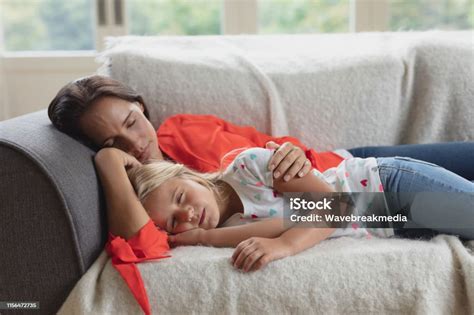 Mother And Daughter Sleeping Together On A Sofa In Living Room Stock