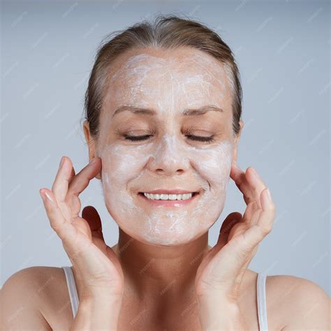 Una mujer madura se aplica una mascarilla cosmética en el rostro y