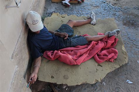 A crack addict sits on a sidewalk in a residential neighborhood of