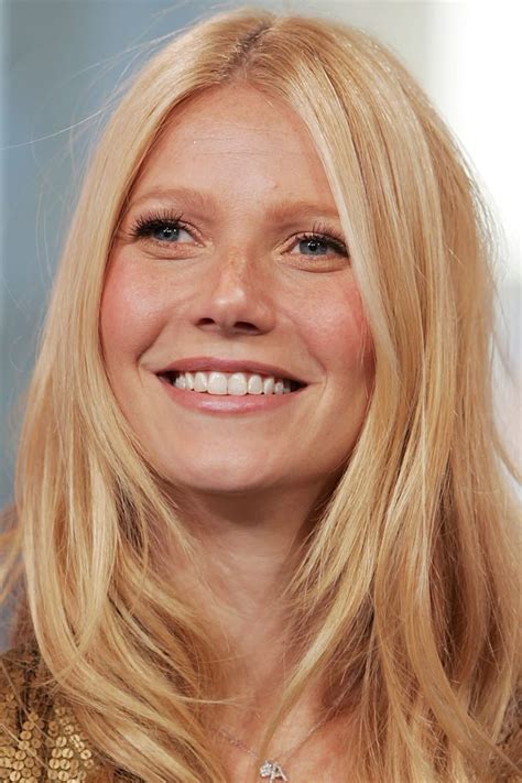 a woman with long blonde hair smiling at the camera and wearing a gold ...