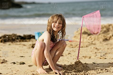 Young girl squatting on a sandy beach stock photo - OFFSET