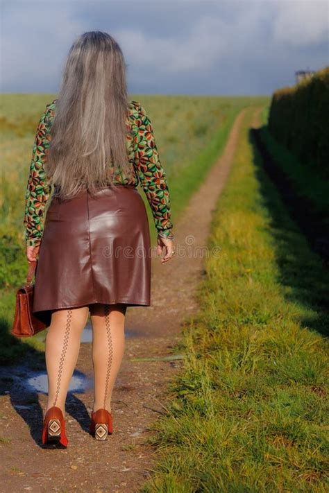 Rear View of Elegant Mature Woman Walking Along a Path in Countryside