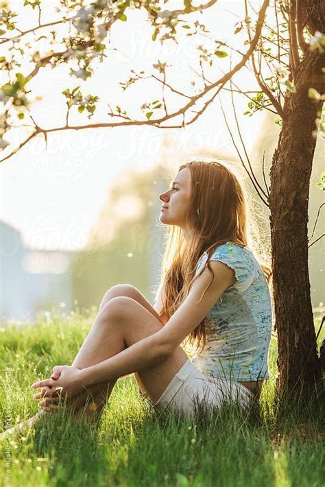 a woman sitting in the grass next to a tree with her eyes closed and ...