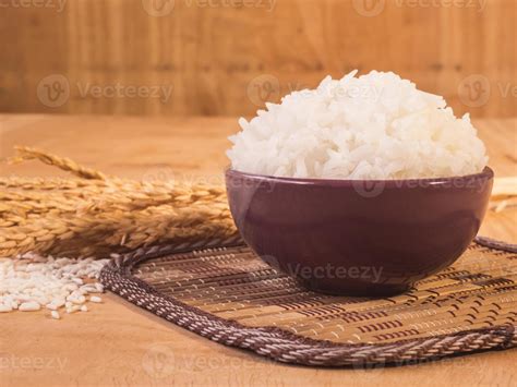 Cooked rice in bowl with raw rice grain and dry rice plant on wooden