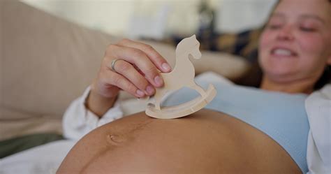 Up close a woman plays with a small wooden toy on her belly while
