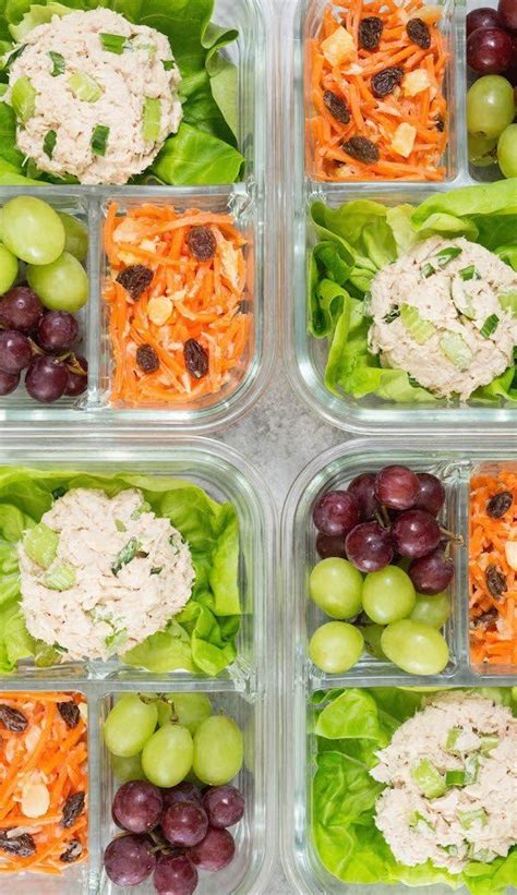 four plastic containers filled with different types of food including grapes, carrots and chicken