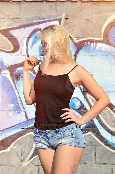 Sexy caucasian blonde girl in denim shorts and black tank top posing