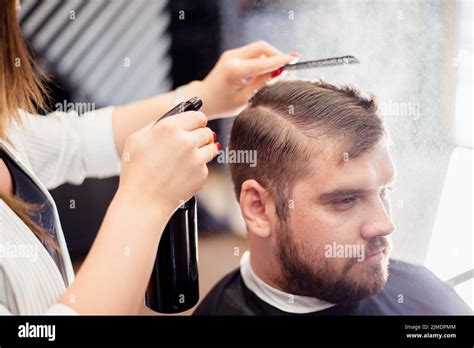Beautiful hairdresser woman doing hairstyle to bearded man in