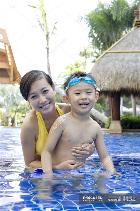 Chino madre e hijo divirtiéndose y mirando en cámara en piscina — niño